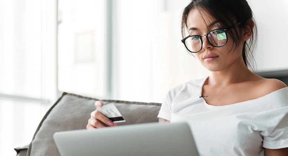 Mulher com cartão em uma de suas mãos e olhando para tela de computador